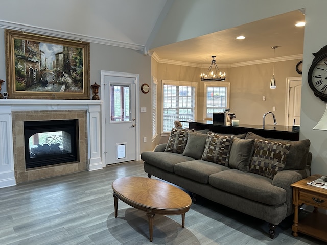 living room featuring hardwood / wood-style floors, a notable chandelier, a tiled fireplace, crown molding, and vaulted ceiling