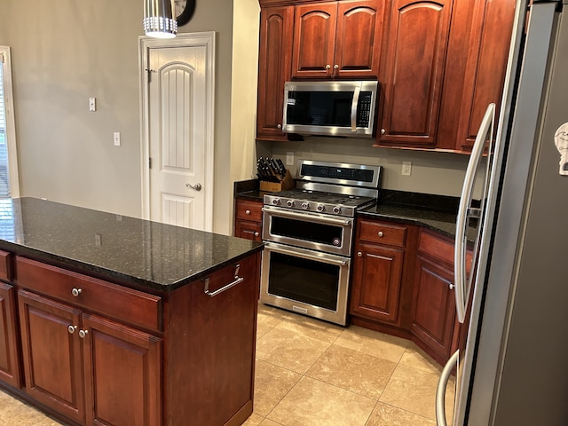 kitchen with a kitchen island, stainless steel appliances, dark stone counters, and light tile patterned flooring