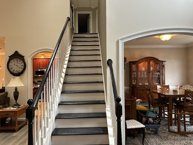 staircase featuring a high ceiling, ornamental molding, and hardwood / wood-style floors