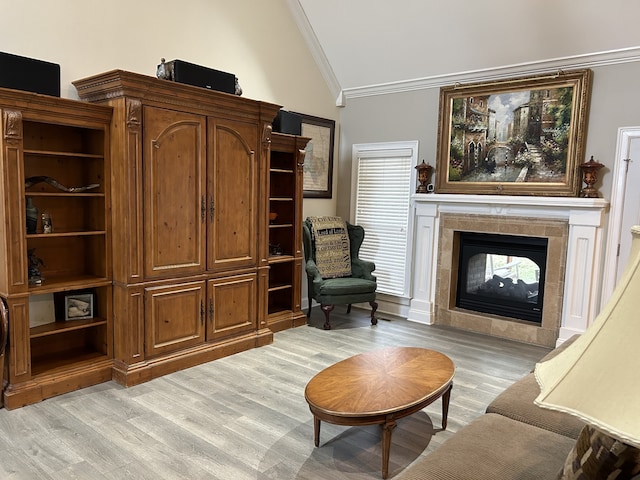 living area with ornamental molding, vaulted ceiling, light hardwood / wood-style floors, and a tile fireplace