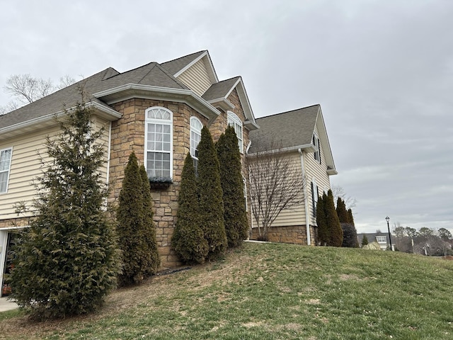 view of home's exterior with a lawn, stone siding, and a shingled roof
