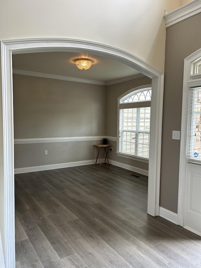 spare room featuring arched walkways, ornamental molding, plenty of natural light, and wood finished floors