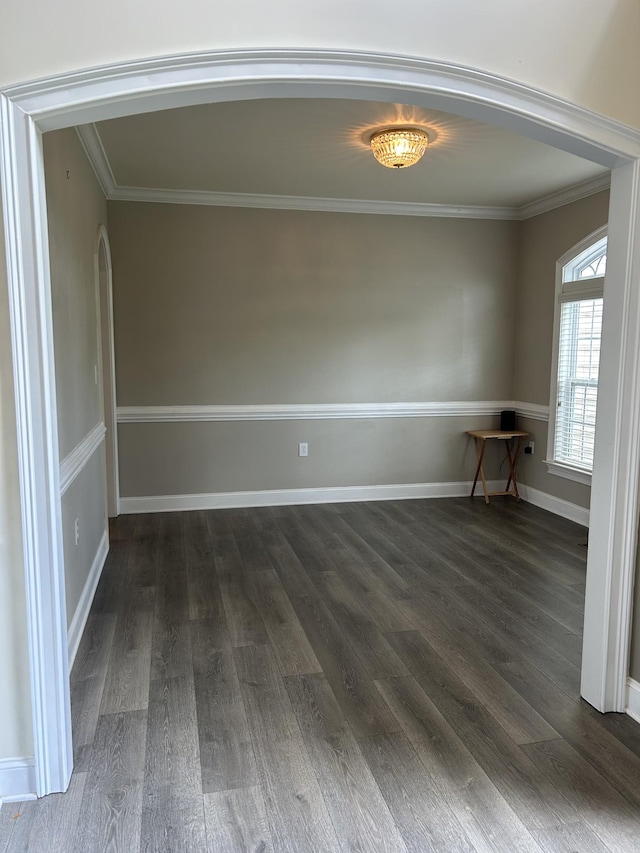 spare room featuring crown molding, arched walkways, dark wood-type flooring, and baseboards