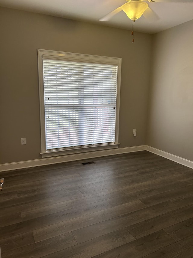 unfurnished room featuring a wealth of natural light, dark wood-type flooring, baseboards, and ceiling fan