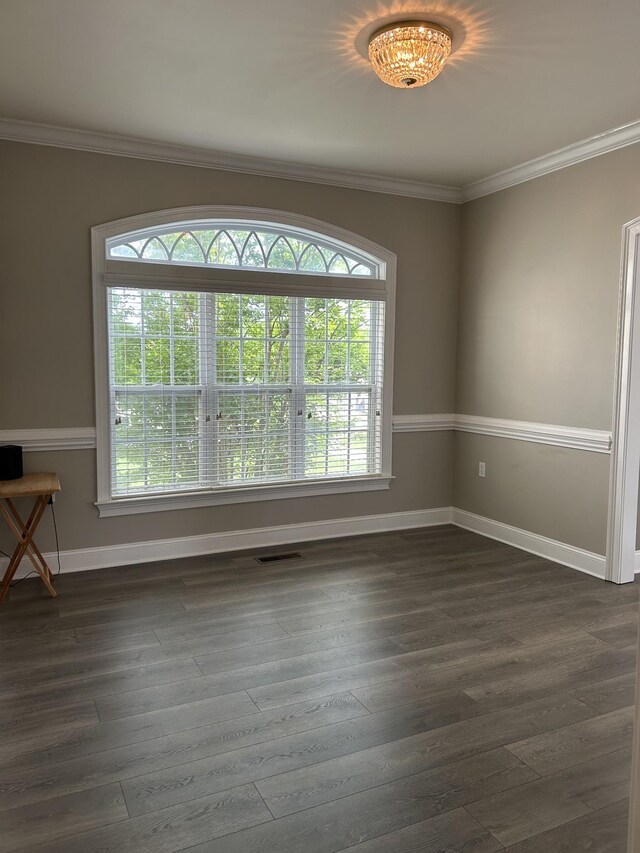 empty room featuring crown molding, baseboards, dark wood-type flooring, and visible vents