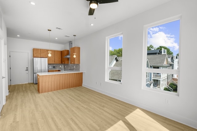 kitchen with light hardwood / wood-style flooring, hanging light fixtures, kitchen peninsula, stainless steel appliances, and ceiling fan