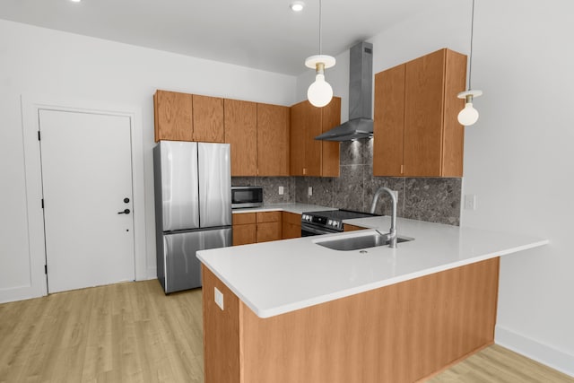 kitchen featuring hanging light fixtures, stainless steel appliances, light hardwood / wood-style flooring, and wall chimney exhaust hood