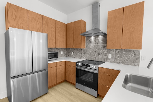 kitchen featuring light wood-type flooring, stainless steel appliances, sink, wall chimney range hood, and decorative backsplash