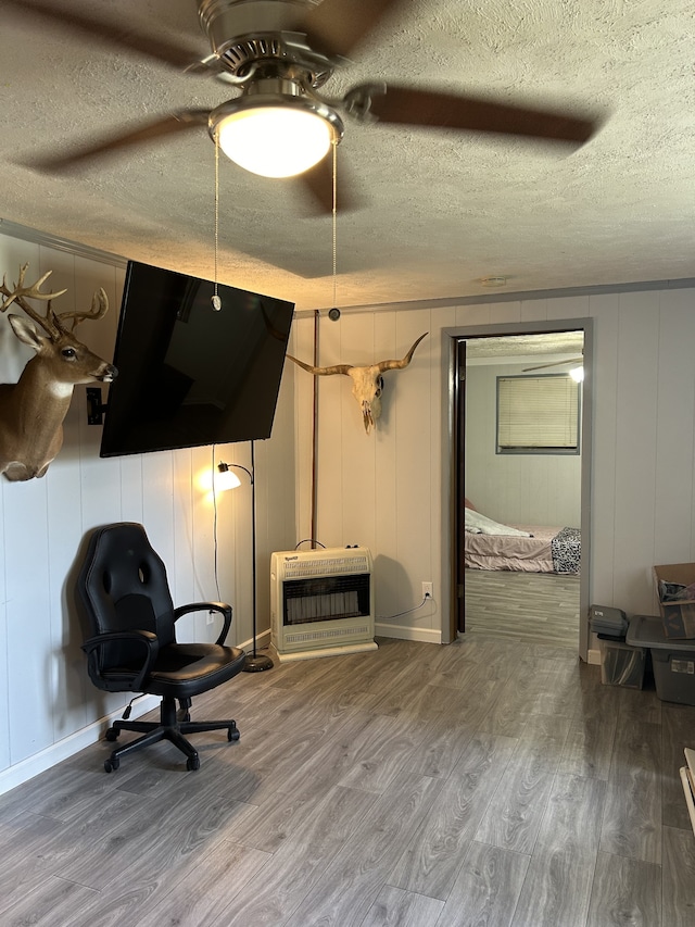 living area with a textured ceiling, hardwood / wood-style flooring, heating unit, and ceiling fan