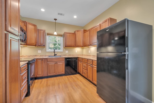 kitchen with hanging light fixtures, light hardwood / wood-style flooring, light stone counters, sink, and black appliances