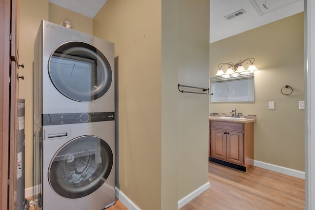 laundry room with sink, light hardwood / wood-style floors, and stacked washer / dryer