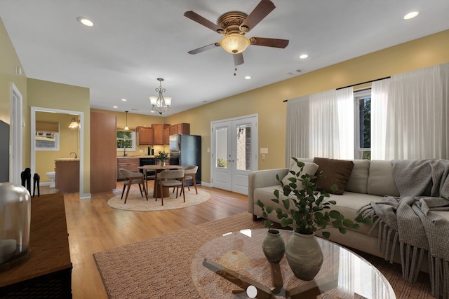 living room with ceiling fan with notable chandelier, light hardwood / wood-style flooring, and sink