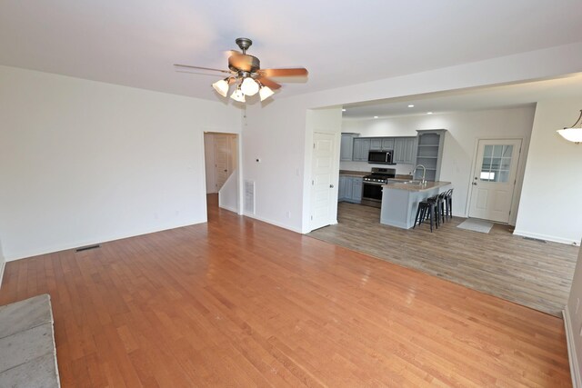 unfurnished living room with sink, hardwood / wood-style floors, and ceiling fan