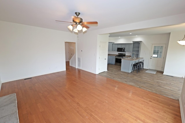 unfurnished living room with a ceiling fan, light wood-type flooring, visible vents, and a sink