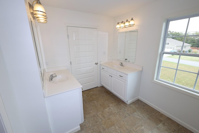 full bath featuring baseboards, two vanities, and a sink