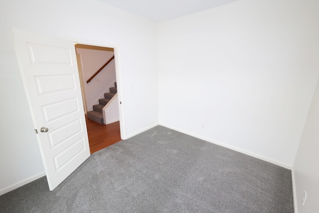 spare room featuring dark colored carpet, baseboards, and stairs