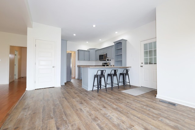 kitchen featuring a peninsula, light wood-type flooring, open shelves, and gray cabinetry