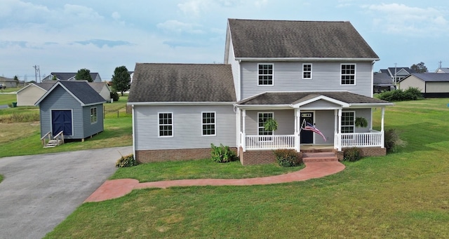 view of front of house with an outbuilding, aphalt driveway, covered porch, a shingled roof, and a front yard