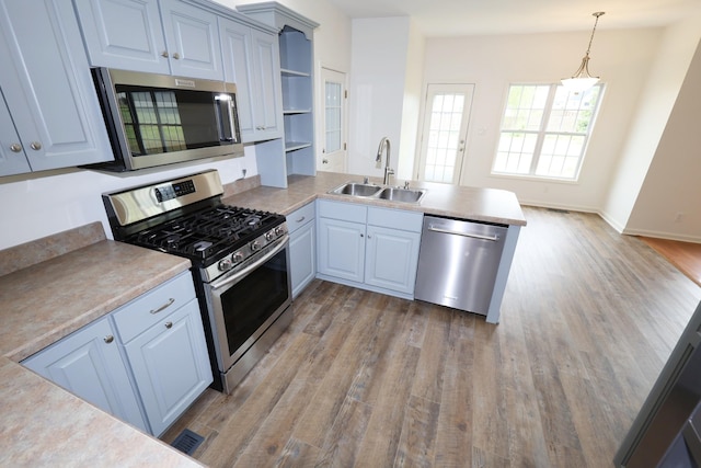 kitchen with stainless steel appliances, a peninsula, wood finished floors, a sink, and open shelves