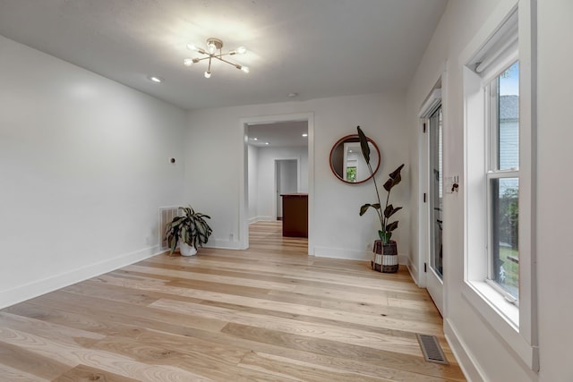 spare room with a healthy amount of sunlight, an inviting chandelier, and light hardwood / wood-style floors