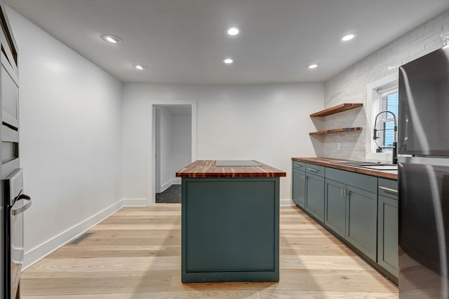 kitchen with stainless steel refrigerator, light hardwood / wood-style flooring, wood counters, a center island, and sink