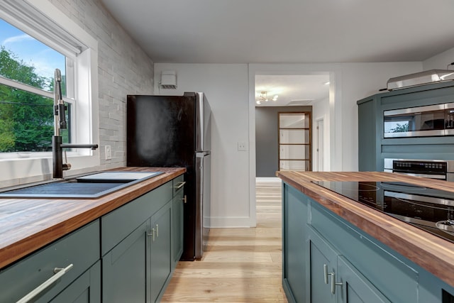 kitchen with light wood-type flooring, appliances with stainless steel finishes, butcher block counters, and sink