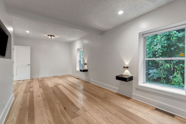 unfurnished room featuring a textured ceiling, plenty of natural light, and light hardwood / wood-style flooring