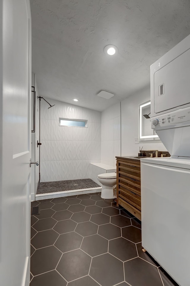 bathroom with toilet, tile patterned flooring, vanity, tiled shower, and stacked washer / drying machine