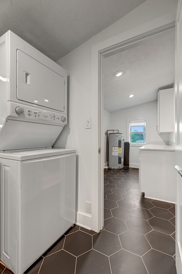 clothes washing area with dark tile patterned flooring, stacked washer and dryer, a textured ceiling, and water heater