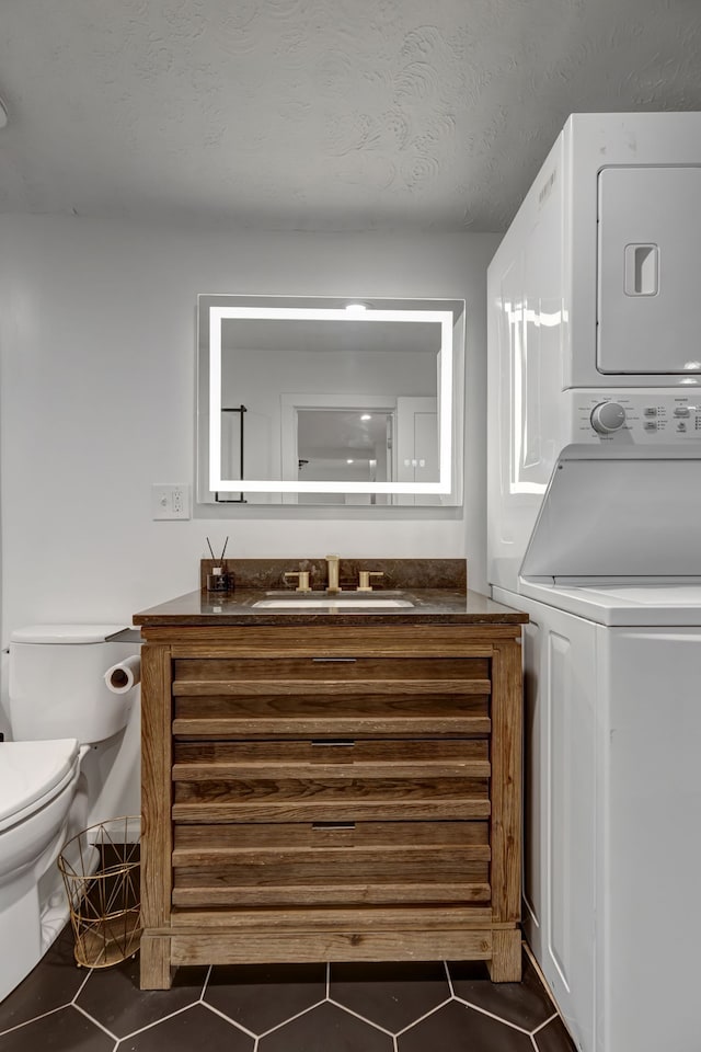 laundry area featuring a textured ceiling, dark tile patterned floors, stacked washer and clothes dryer, and sink