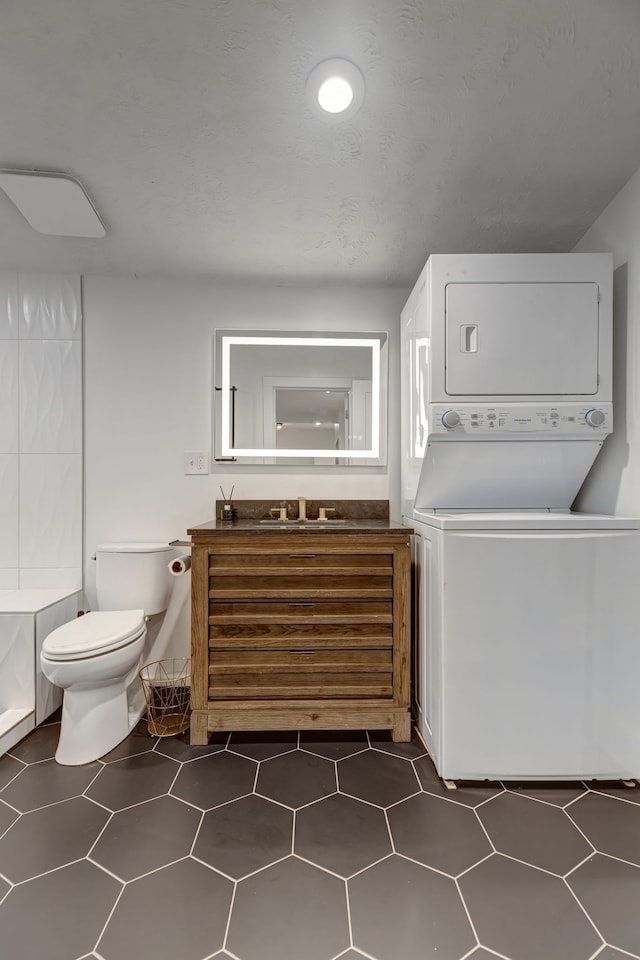 laundry room with dark tile patterned flooring, stacked washer / drying machine, and sink