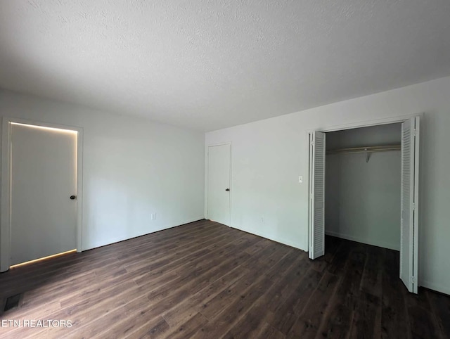 unfurnished bedroom with a textured ceiling, dark wood-type flooring, and a closet