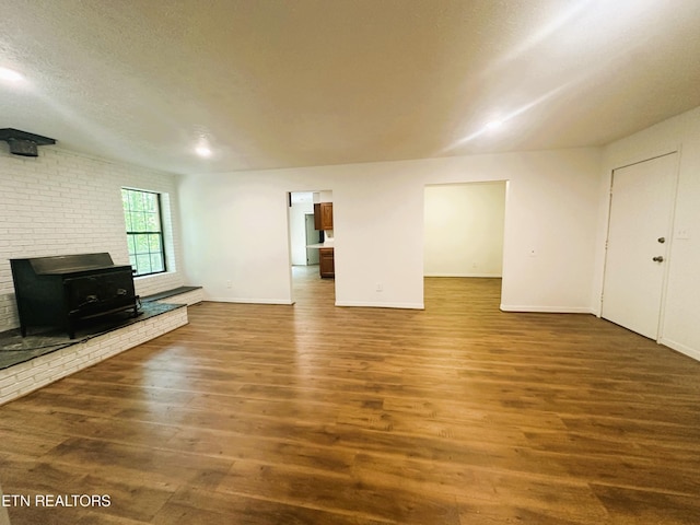 unfurnished living room with wood-type flooring, a wood stove, and a textured ceiling