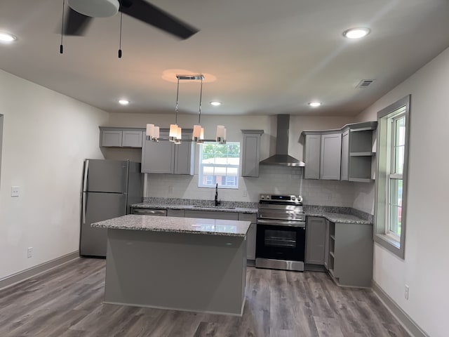 kitchen featuring hardwood / wood-style flooring, decorative light fixtures, appliances with stainless steel finishes, wall chimney exhaust hood, and a kitchen island