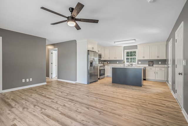 kitchen with stainless steel appliances, a center island, ceiling fan, white cabinets, and light hardwood / wood-style floors