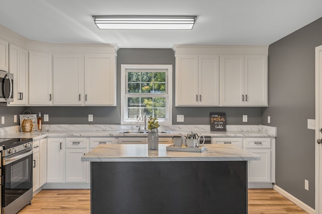 kitchen featuring white cabinets, light hardwood / wood-style flooring, light stone countertops, stainless steel appliances, and a kitchen island