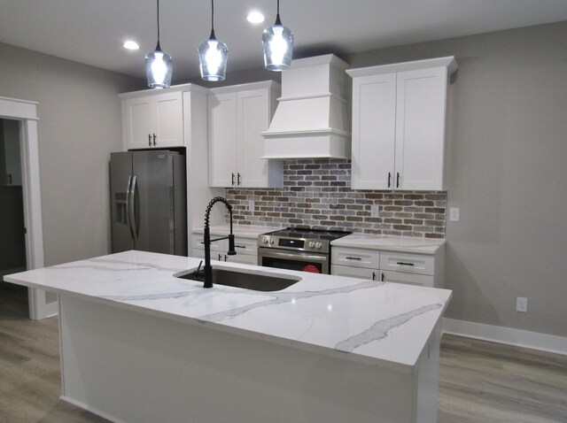 kitchen with decorative light fixtures, premium range hood, stainless steel appliances, and a kitchen island with sink