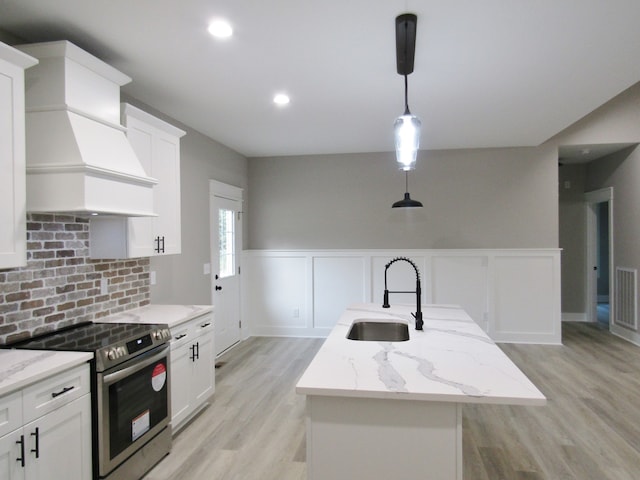 kitchen featuring white cabinets, light hardwood / wood-style floors, sink, electric stove, and an island with sink