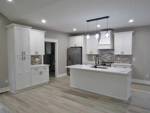 kitchen featuring a kitchen island with sink, custom exhaust hood, sink, stainless steel fridge with ice dispenser, and white cabinets