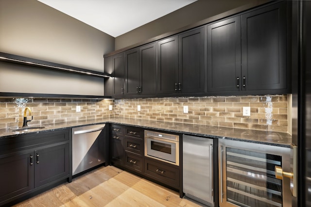 kitchen with sink, stainless steel appliances, beverage cooler, tasteful backsplash, and dark stone countertops