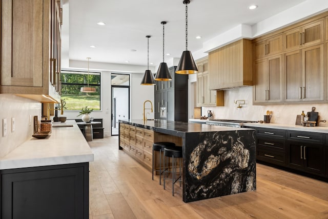 kitchen featuring pendant lighting, custom exhaust hood, light wood-type flooring, and a large island with sink