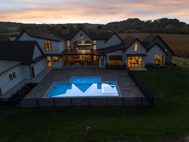 pool at dusk featuring a patio and a lawn