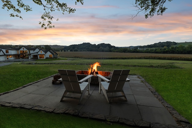 patio terrace at dusk featuring a lawn, a rural view, and an outdoor fire pit