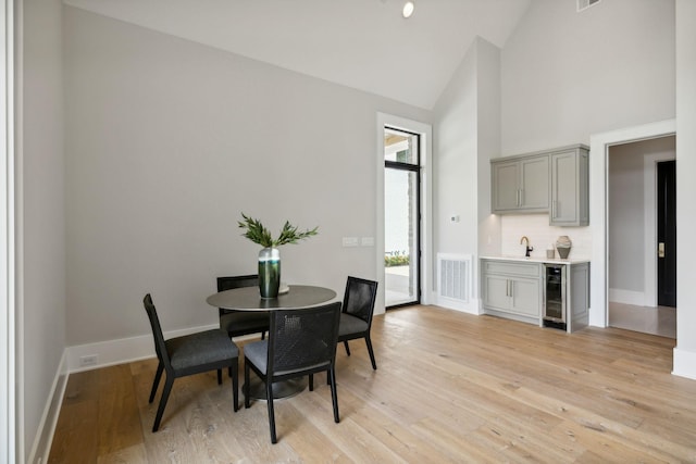 dining space featuring high vaulted ceiling, light hardwood / wood-style flooring, beverage cooler, and sink