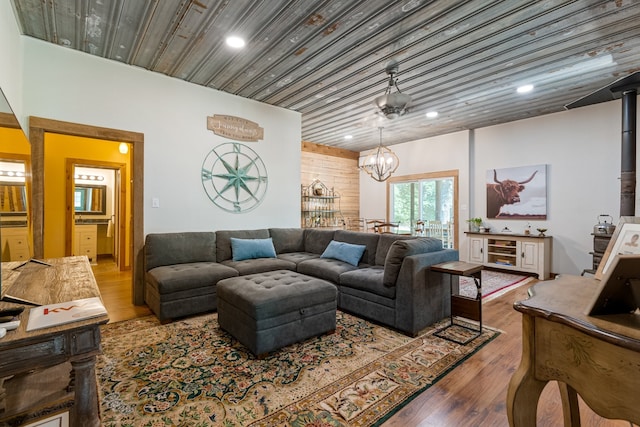 living room with wood walls, wooden ceiling, a wood stove, a notable chandelier, and wood-type flooring