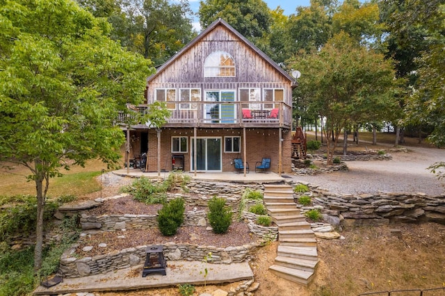 back of house featuring brick siding, a patio, a fire pit, a wooden deck, and stairs