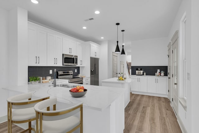 kitchen with hanging light fixtures, light wood-type flooring, light stone countertops, stainless steel appliances, and kitchen peninsula