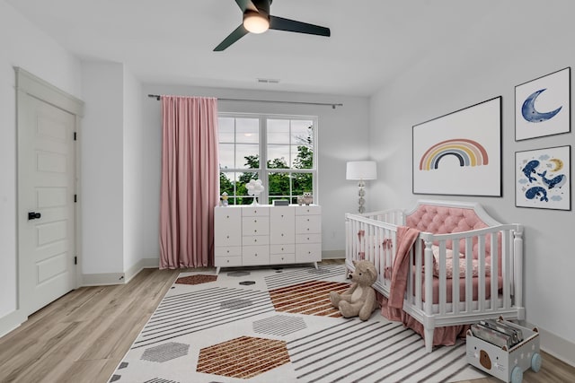 bedroom featuring visible vents, a ceiling fan, wood finished floors, a crib, and baseboards