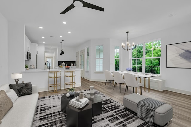 living area with baseboards, ceiling fan with notable chandelier, light wood-type flooring, and recessed lighting