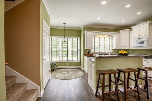 kitchen with ornamental molding, a kitchen bar, decorative light fixtures, dark wood-type flooring, and white cabinets